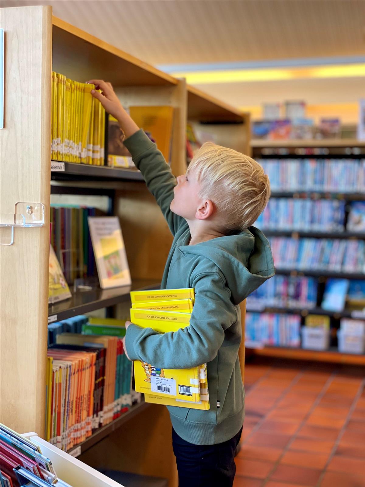 Bilde av barn som ser i bokhyller på biblioteket - Klikk for stort bilde