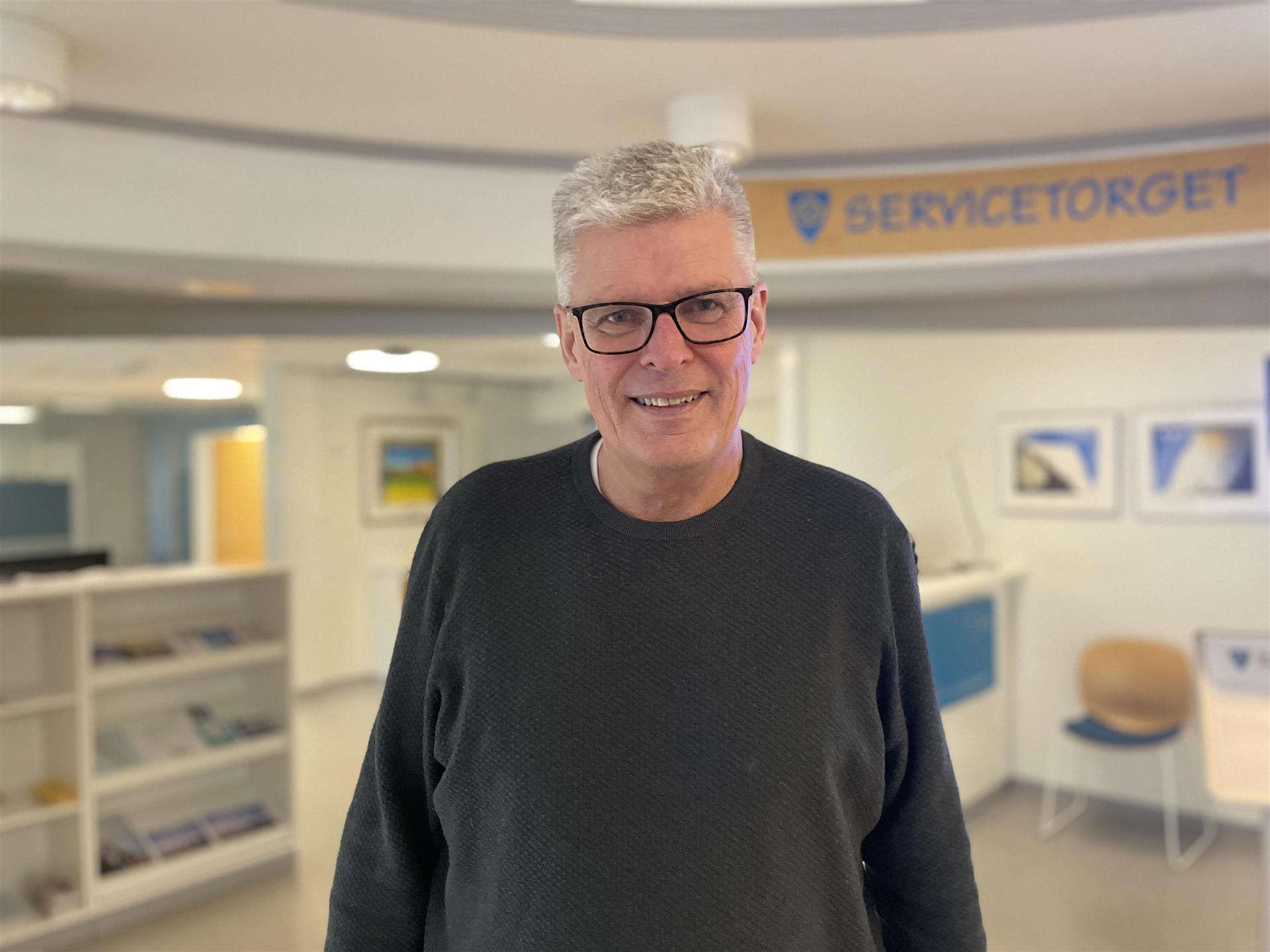 Bildet av ordfører Petter Jørgensen som smiler. I bagrunnen ser man Servicetorget på rådhuset.